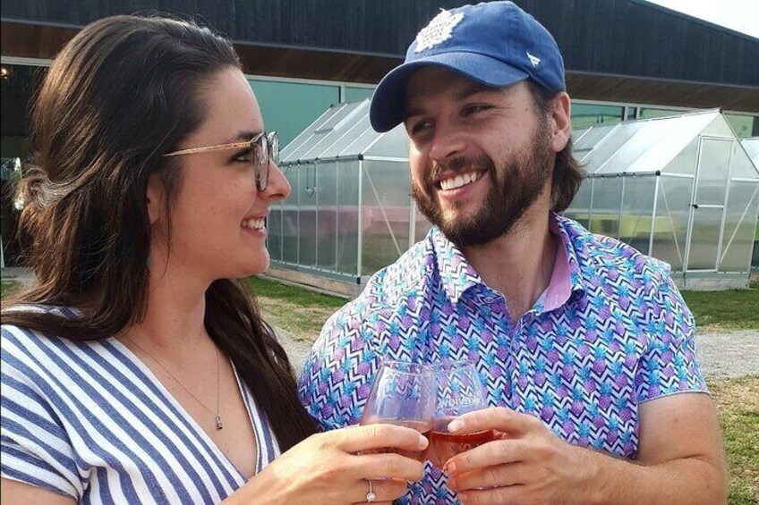 Two people holding a glass of wine in front of a greenhouse. 1