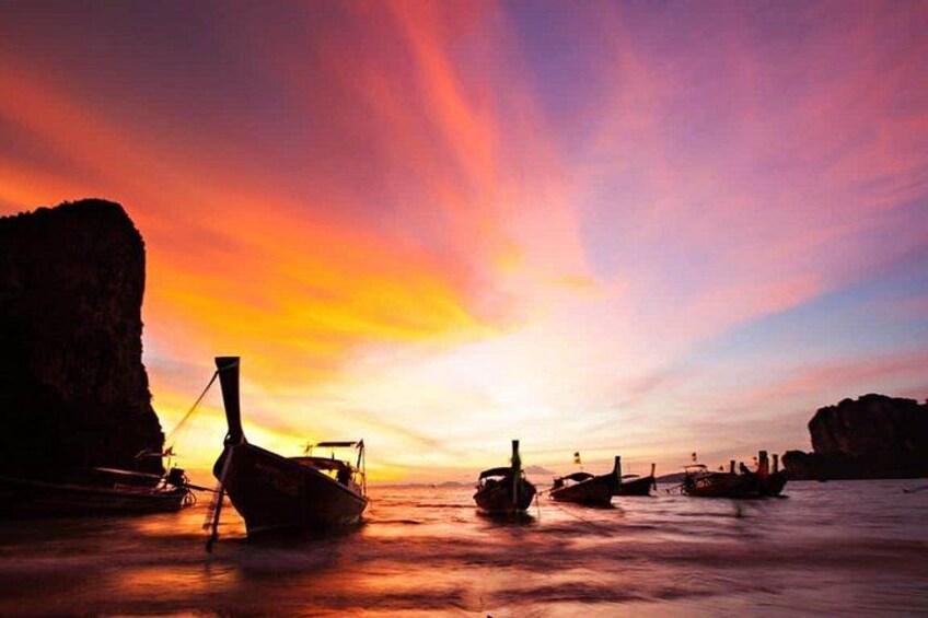 A sunset over a calm sea with boats anchored near rocky cliffs. 5