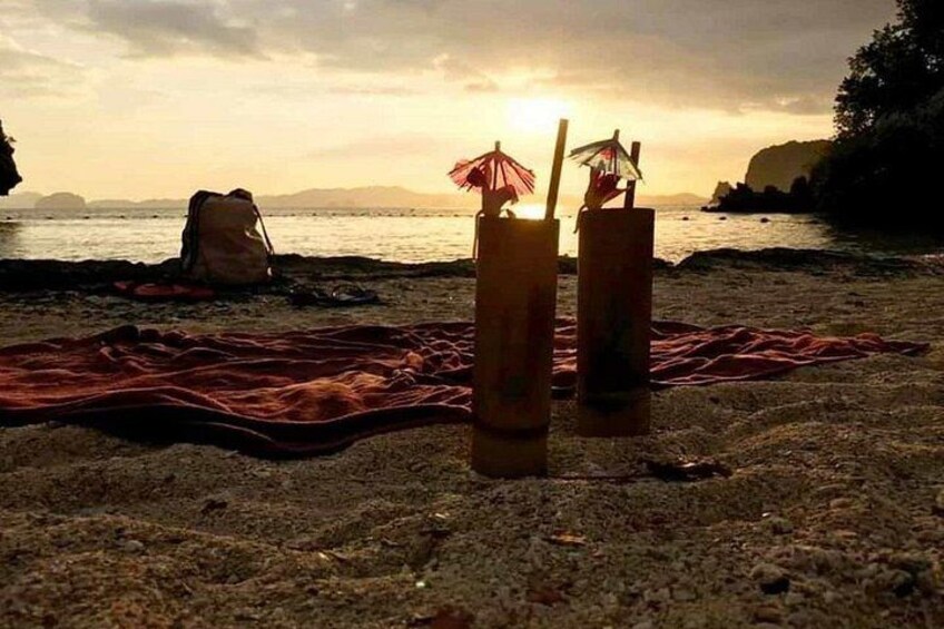A beach with drinks in glasses, a blanket, and a sunset. 4