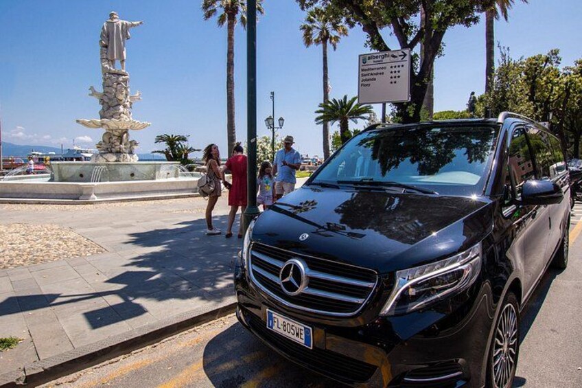 A black Mercedes-Benz SUV parked near a fountain with people walking around. 2