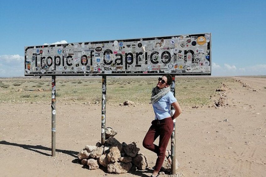 A sign with stickers, a person standing next to it, and a rocky area in the background. 3