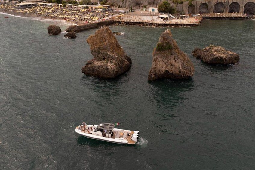 A boat on calm water with rocky formations and a beach with umbrellas in the background. 2