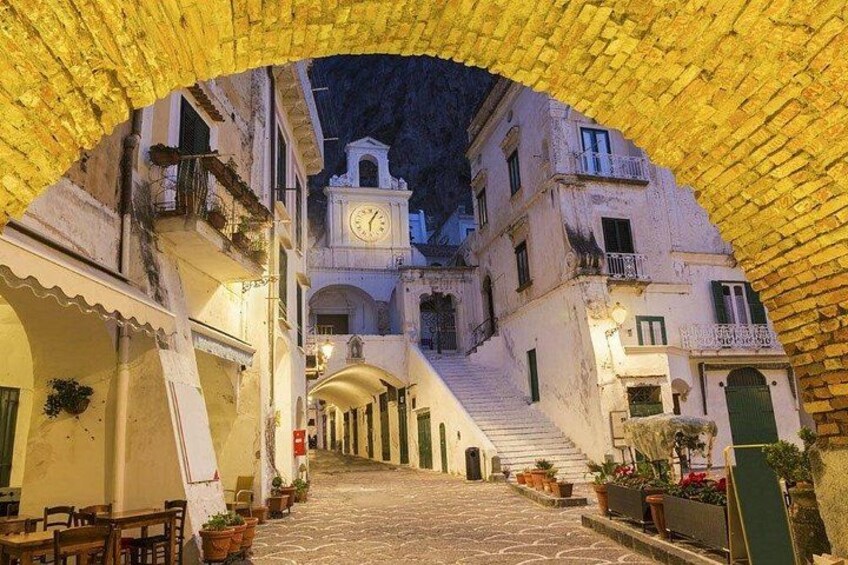 A narrow street with buildings on either side, a clock tower, and a brick archway. 5