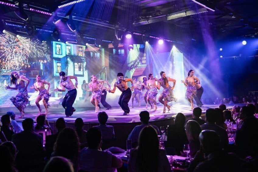 A dance performance on a stage with a cityscape backdrop and audience seated in front. 1
