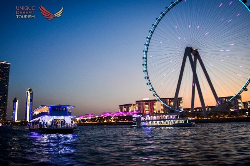 A large Ferris wheel, a river, and a brightly lit building with a boat. 5