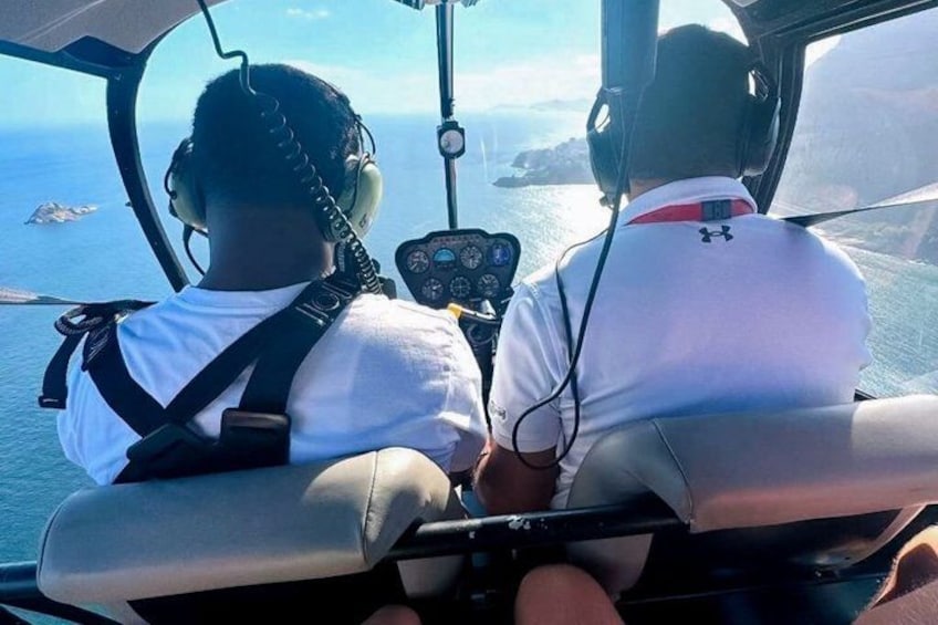 Two people in a helicopter cockpit with a view of the ocean and a ship in the distance. 4