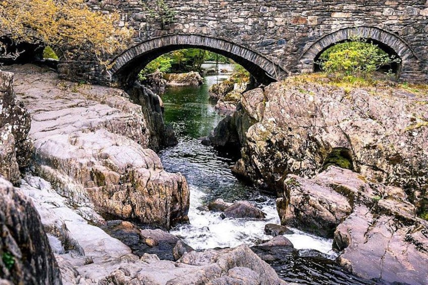 A stone bridge over a river with large rocks in the foreground. 1