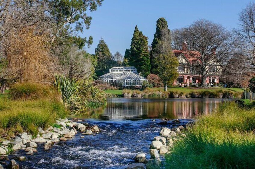 Ein Fluss fließt durch einen Park, im Hintergrund sind ein Gewächshaus und ein Gebäude zu sehen. 1