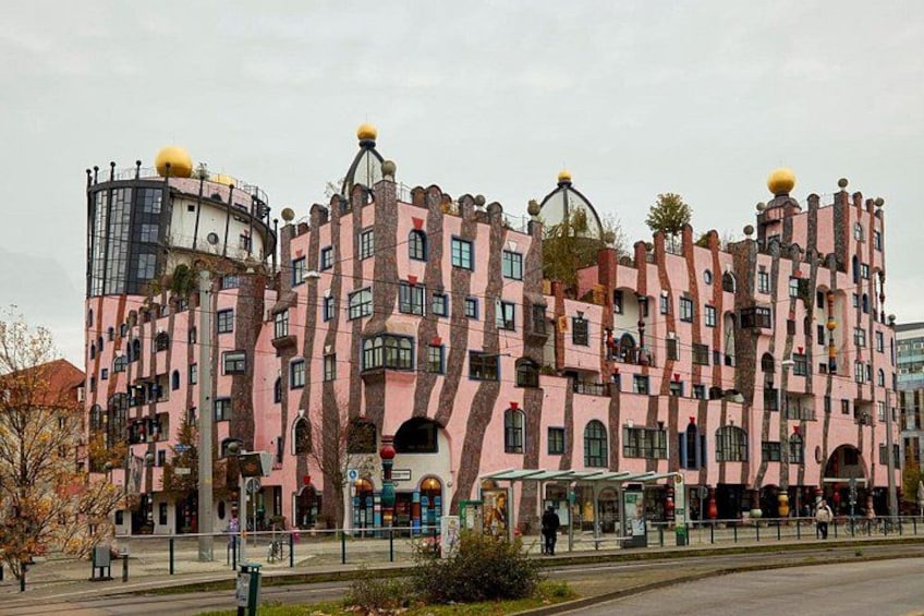 A pink and yellow building with unique architecture, a bus stop, and a pedestrian walkway. 3