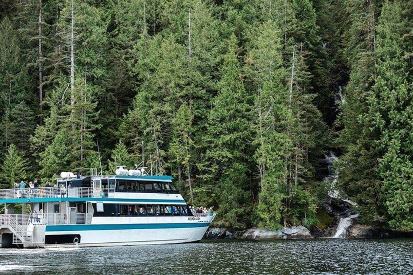Een boot met passagiers, omringd door dicht bos en een waterval. 2