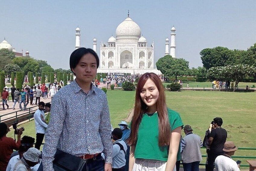 Dos personas de pie frente al Taj Mahal, con una multitud de fondo. 2