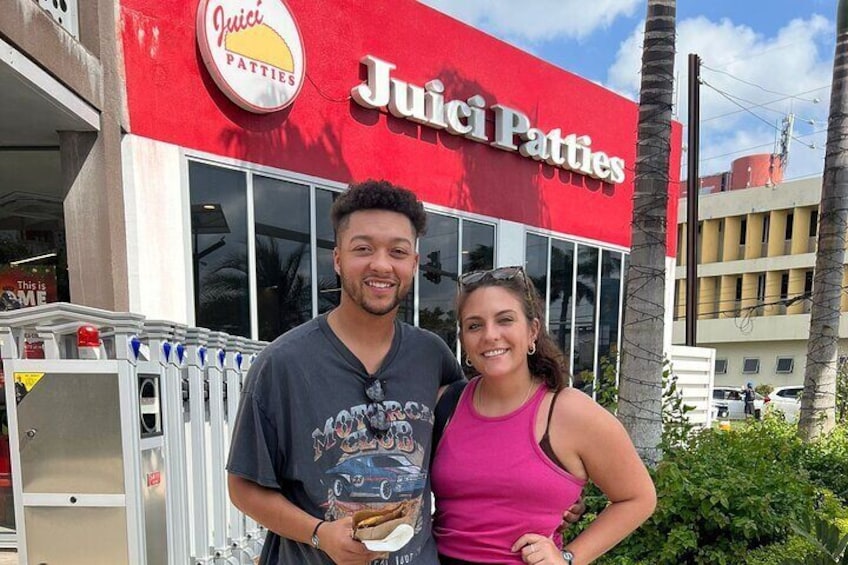 A Juici Patties restaurant with a red facade and a sign, palm trees, and a clear sky in the background. 3