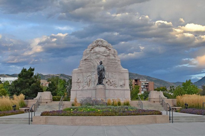 Un monumento de piedra con una estatua, rodeado por un jardín ajardinado con senderos. 3