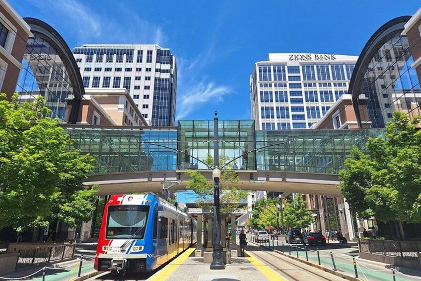 Un tren en una estación con un puente peatonal y edificios modernos al fondo. 2