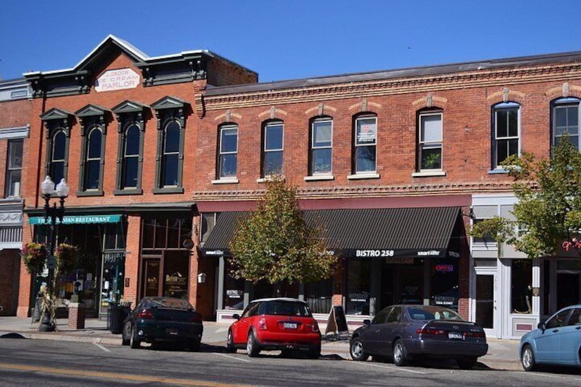A street with brick buildings, parked cars, and storefronts. 4