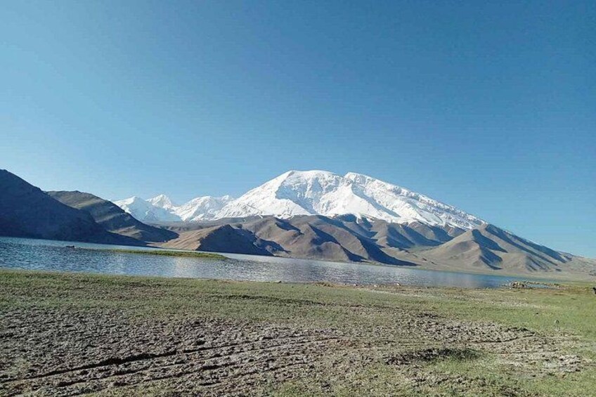 A mountain range with a snow-capped peak, a lake, and a grassy foreground. 3