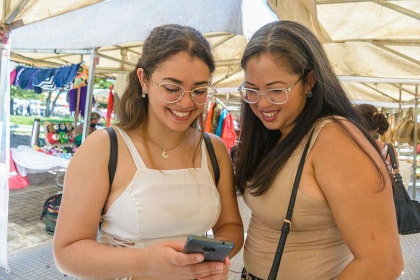 Two people at an outdoor market with tents and various items on display. 4