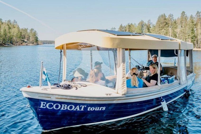 En båd med teksten 'ECOBOAT tours' på siden, passagerer ombord og et roligt vandareal med træer i baggrunden. 1