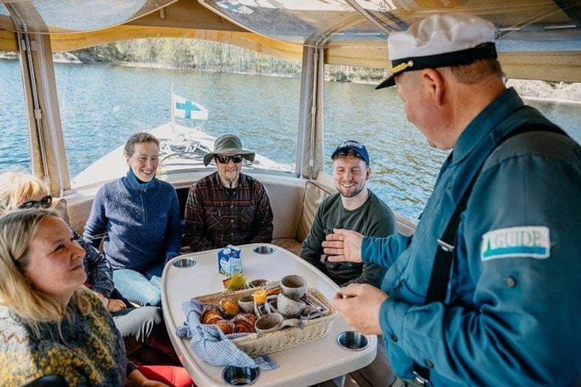 En gruppe mennesker på en båd med en guide, et bord med mad og et vandareal i baggrunden. 4