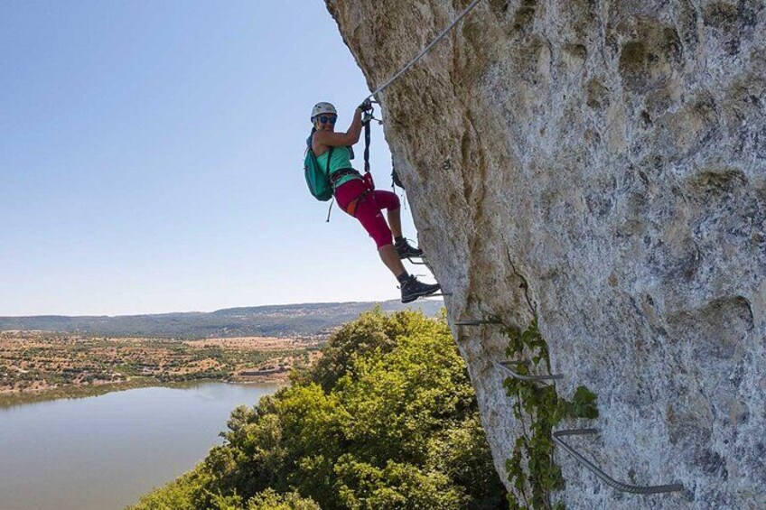 Une personne fait de l’escalade sur une falaise, avec vue sur un lac et la végétation en contrebas. 1