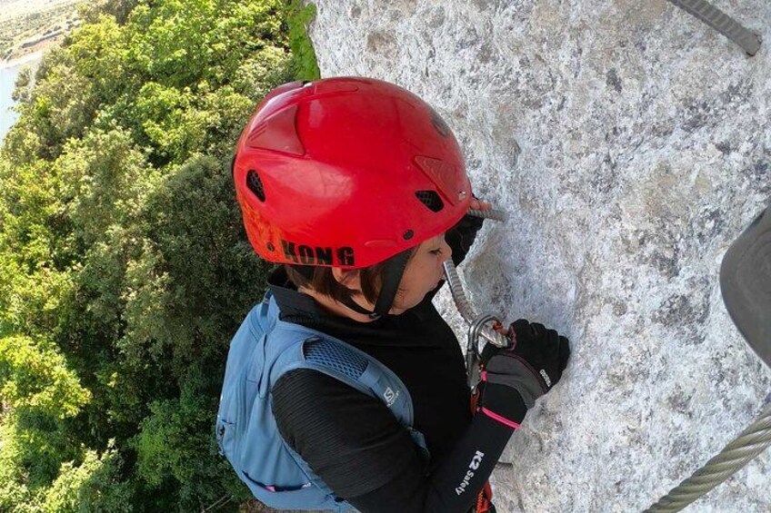 Une personne escalade une paroi rocheuse, portant un casque rouge et un harnais. 2