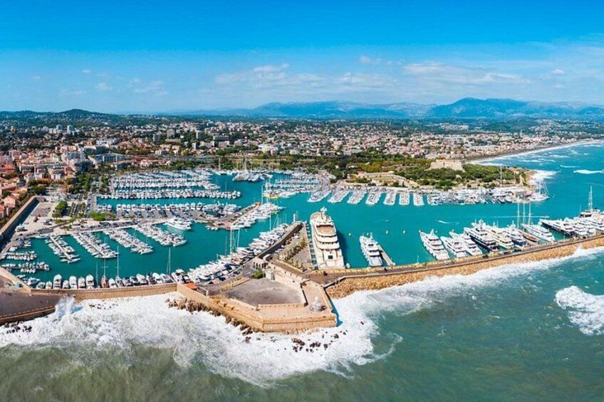 A coastal marina with numerous boats docked, a prominent lighthouse, and a fortified structure. 1