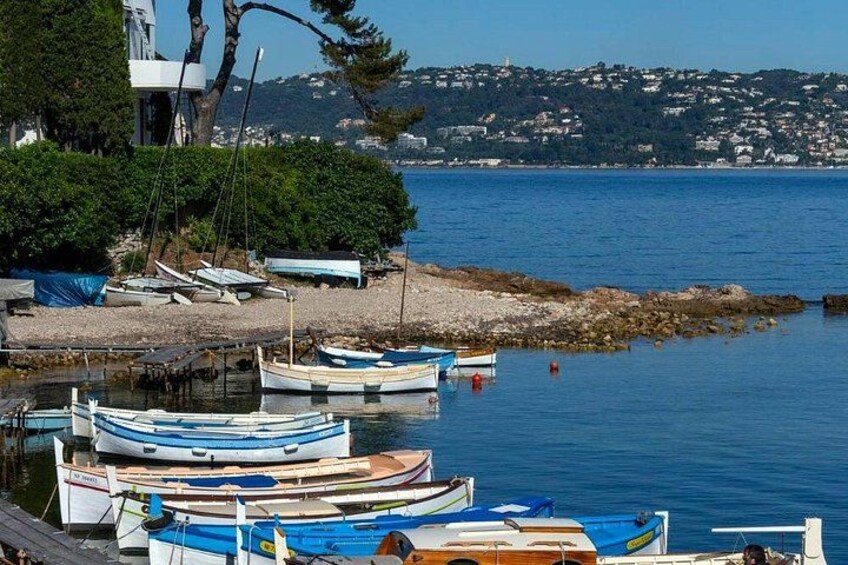 A harbor with several small boats docked, a rocky shoreline, and a distant view of a town across the water. 4