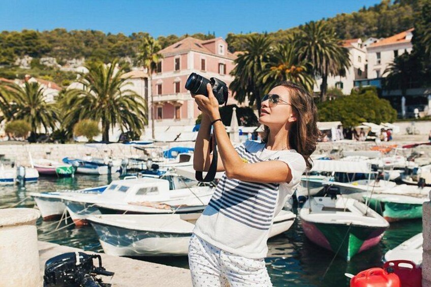 A person taking a photo with a camera at a marina with boats and buildings in the background. 5