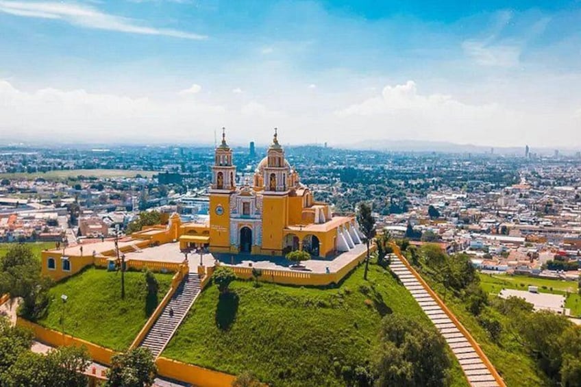 A yellow church with two towers, surrounded by green grass and a cityscape in the background. 1