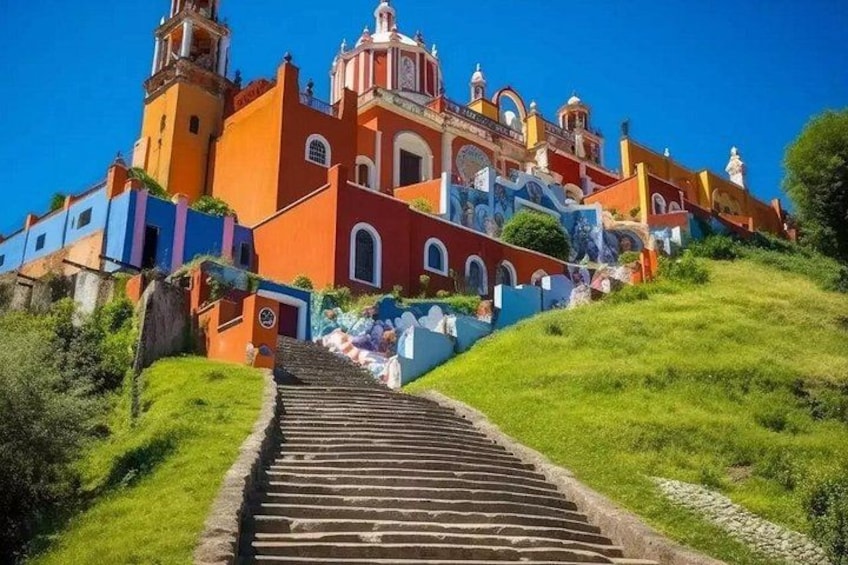 A colorful church with a bell tower, a staircase leading up to it, and a clear blue sky. 4