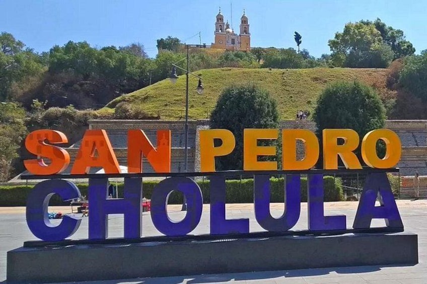 A sign with 'SAN PEDRO CHOLULA' in large letters, with a hill and a church in the background. 5