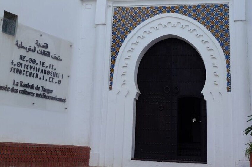 A building with a large black door and a decorative archway. There is a sign on the wall with text in multiple languages. 5