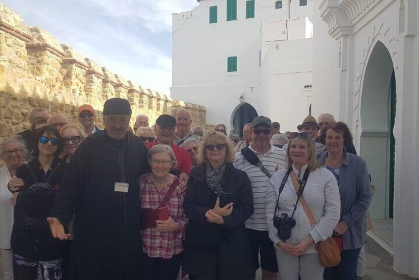 A group of people standing in front of a white building with a stone wall. 2