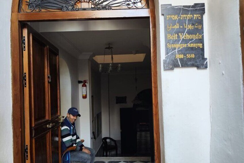 A person sitting on a chair in a doorway, a sign with Hebrew text, and a fire extinguisher on the wall. 3