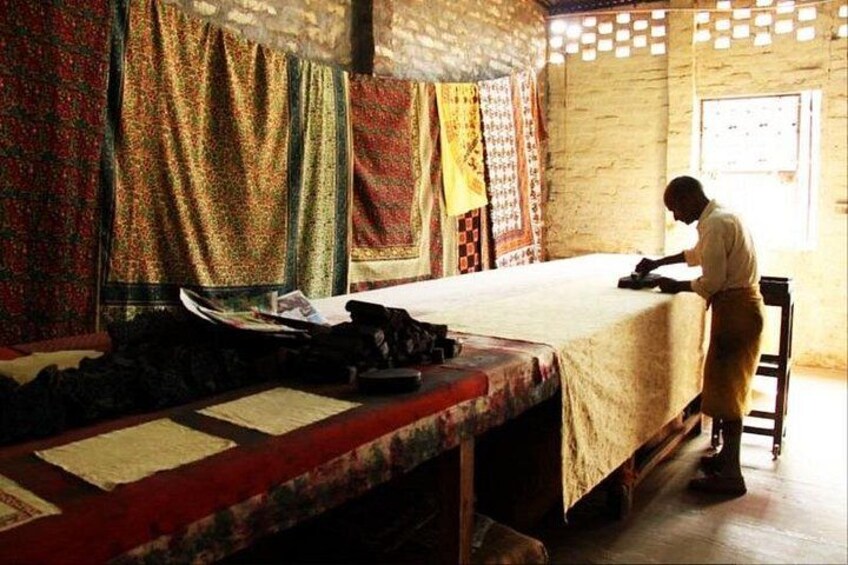 Una habitación con una cama, una persona planchando ropa y cortinas estampadas. 3