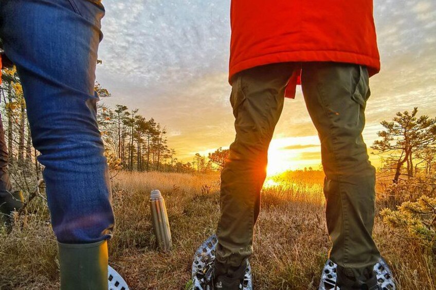Two people standing in a field with a sunset in the background. 1