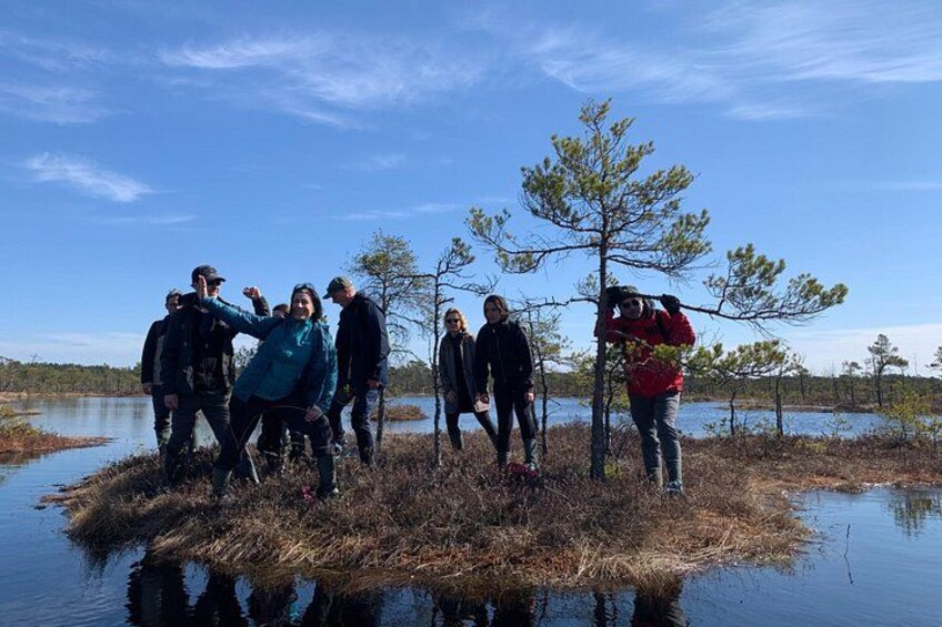 A group of people standing on a small island surrounded by water, with trees and a clear sky in the background. 2