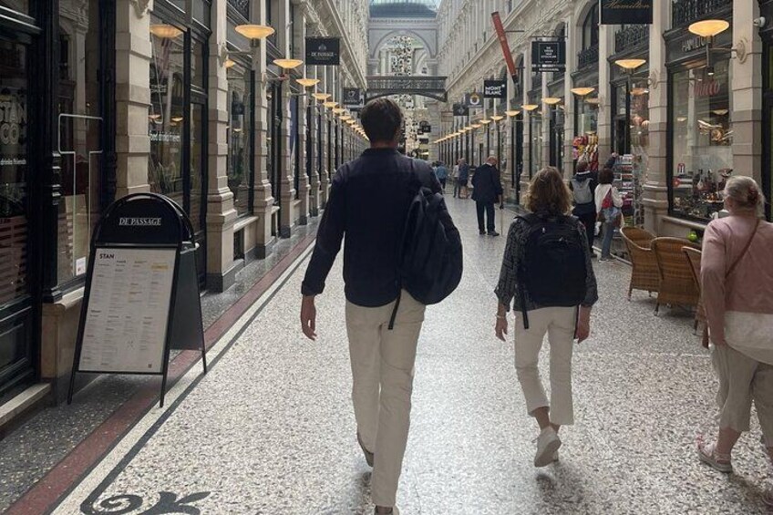 Une promenade piétonne bordée de boutiques des deux côtés, un panneau indicateur et des passants. 3