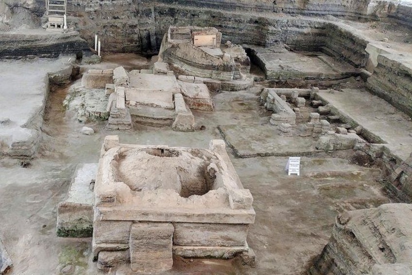Ancient ruins with stone structures and a large central pit. 2