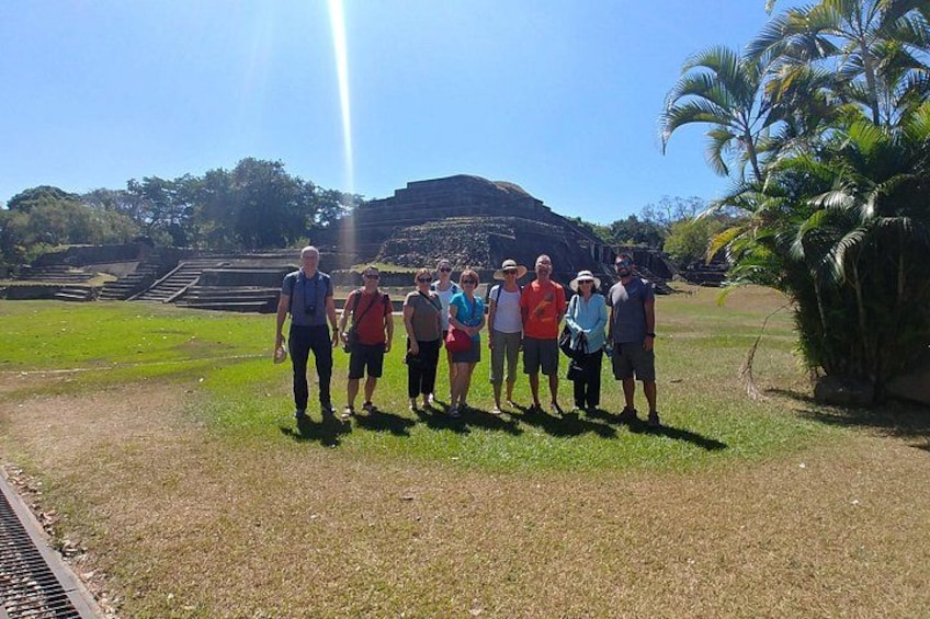 A group of people standing in a grassy area with a large ancient structure in the background. 3