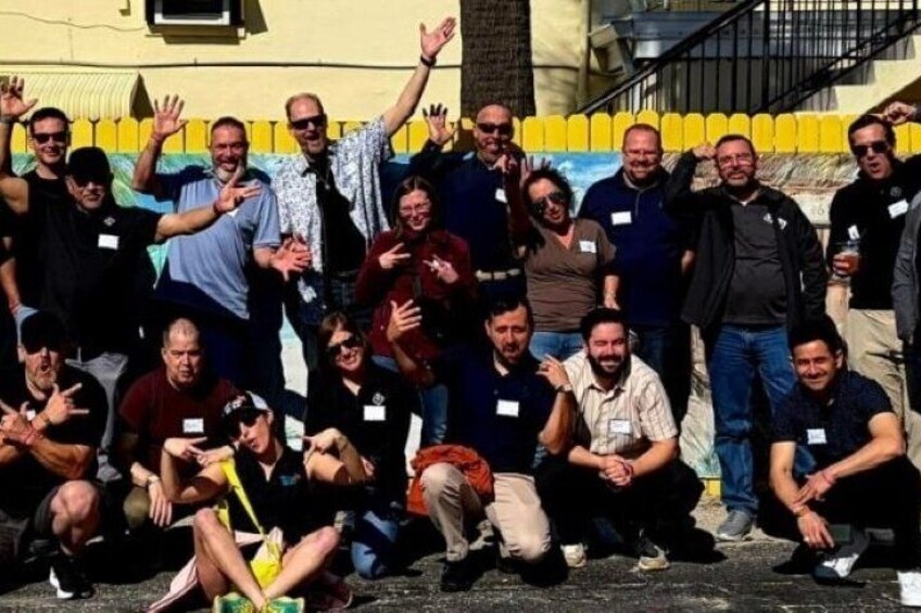 Un groupe de personnes posant pour une photo dans un cadre extérieur, avec un mur à rayures jaunes et blanches en arrière-plan. 5