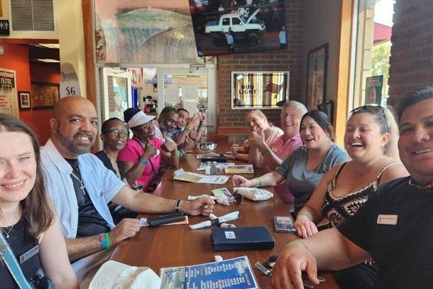 Un groupe de personnes est assis autour d’une table en bois dans un restaurant. On peut voir un menu et une affiche sur le mur indiquant « Bud Light ». 5