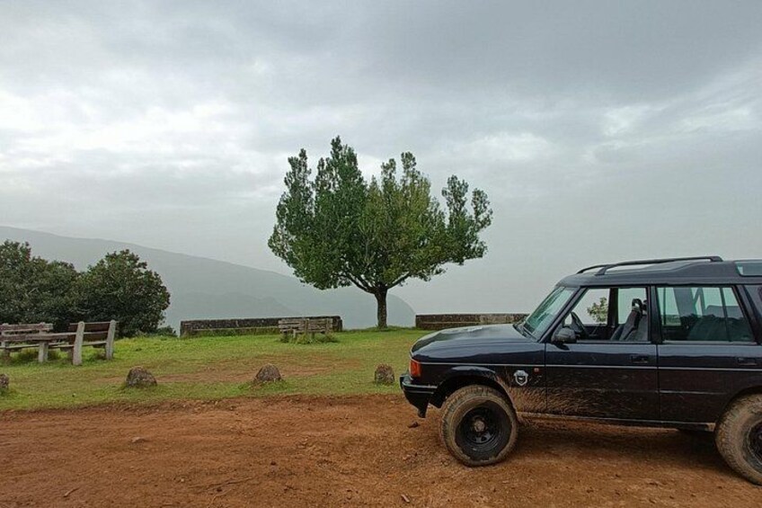 A black SUV parked on a dirt path with a large tree and benches in the background. 5