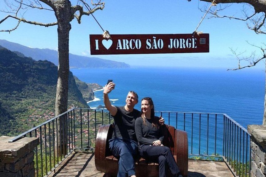 A couple sitting on a bench with a sign above them that reads 'I love Arco São Jorge.' 3