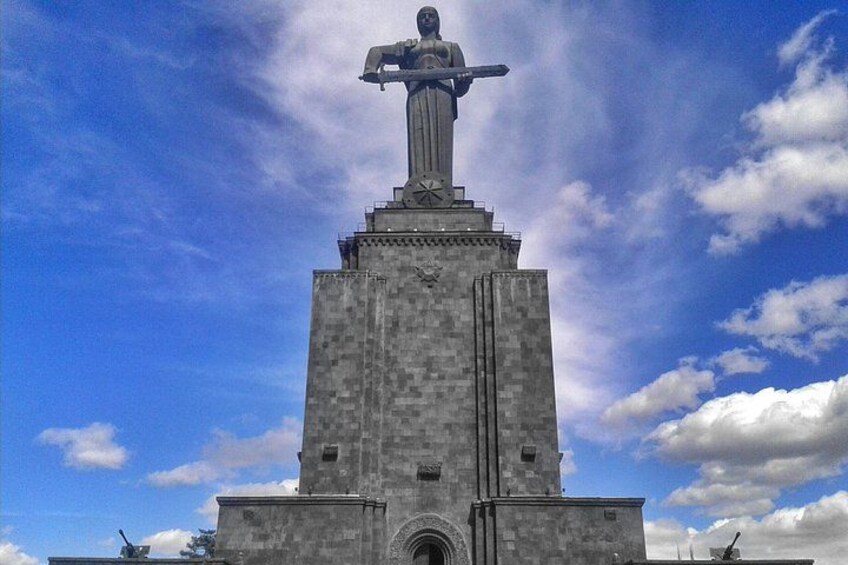A tall monument with a statue on top, set against a blue sky with clouds. 2