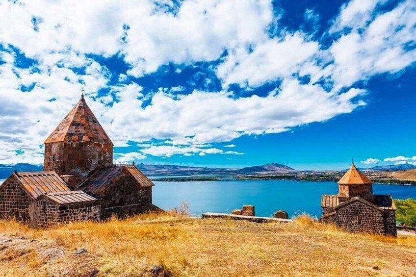 A historic church with a pointed roof, a body of water, and a mountainous landscape in the background. 2