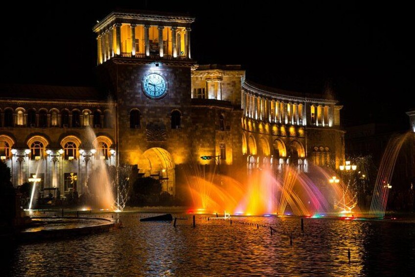 A historic building with a clock tower and illuminated water fountains at night. 5