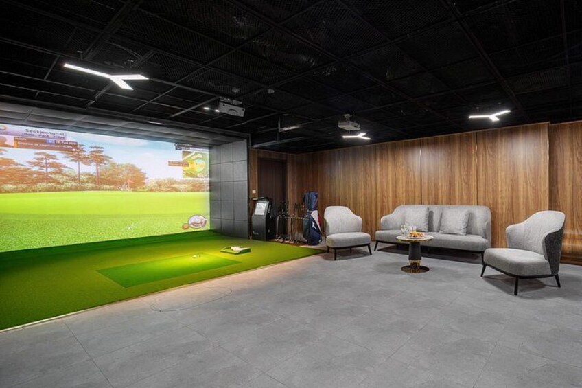 A golf simulation room with a large screen, green turf, and modern furniture. 4