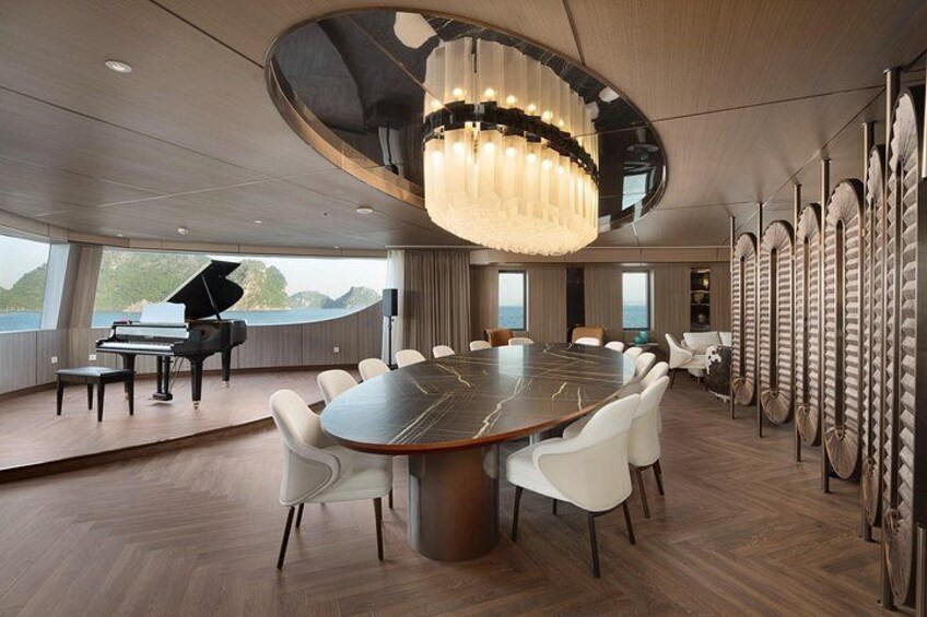 A modern conference room with a large round table, white chairs, a grand piano, and a large chandelier. 2