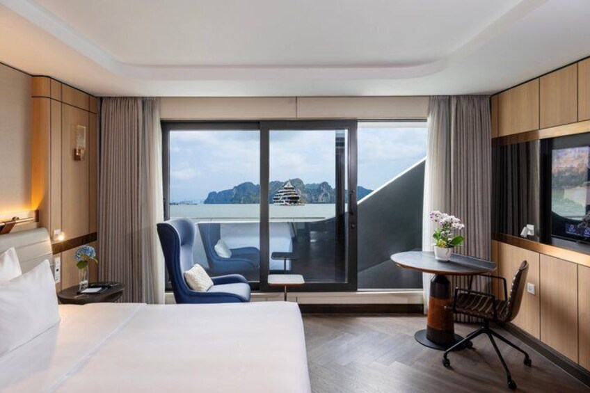 A hotel room with a bed, a desk, a chair, a TV, and a balcony with a view of a body of water and mountains. 2